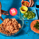 Bowl of Impossible ground pork on a blue background surrounded by small plates of ingredients